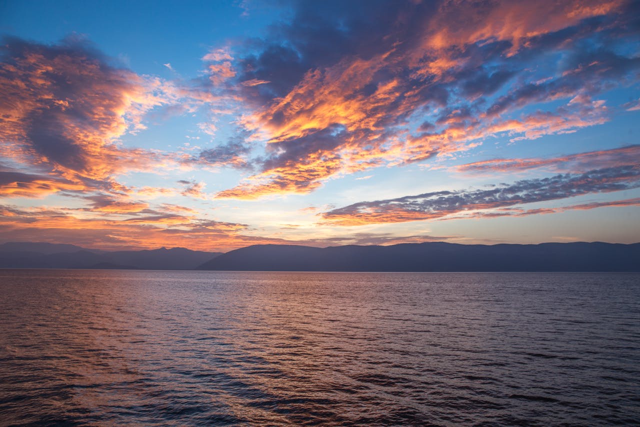 Beyond the Boardwalk: Uncovering the Hidden Gems of the South Jersey Shore A vibrant sunset with dramatic clouds reflects over the calm ocean, capturing natures beauty.